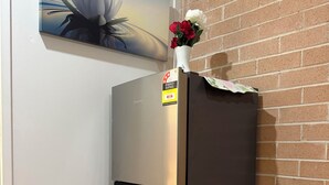 A stainless steel refrigerator with a sticker, placed against a brick wall with a painting above it. - Separate private room In Sydney region (Hebersham)