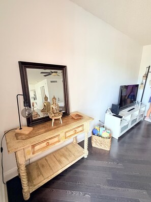 Ein Wohnzimmer mit einem Holztischchen, einem großen Spiegel, einem Fernseher und einem Korbwäscheschrank.