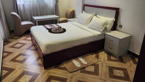 A hotel room with a bed, nightstand, chair, and a small table. - Safe Addis Hotel and Spa (Addis Ababa)