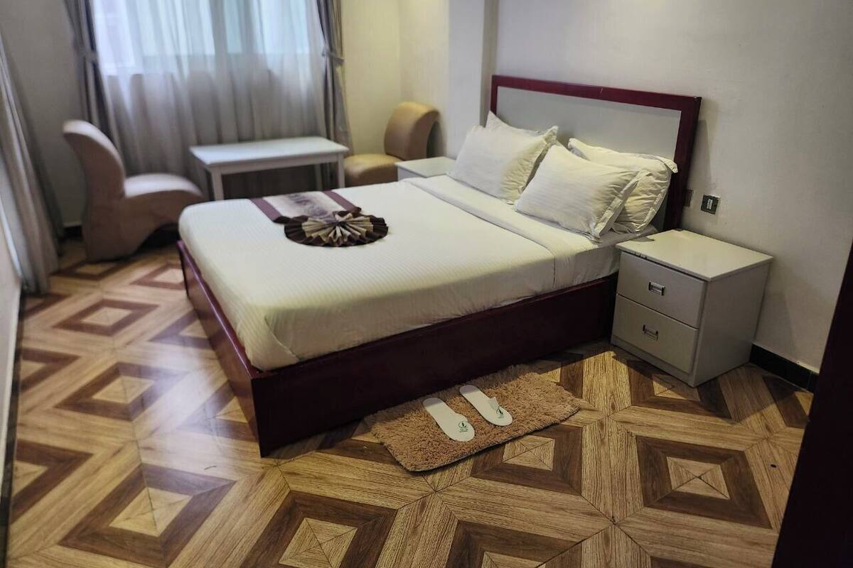 A hotel room with a bed, nightstand, chair, and a small table.
