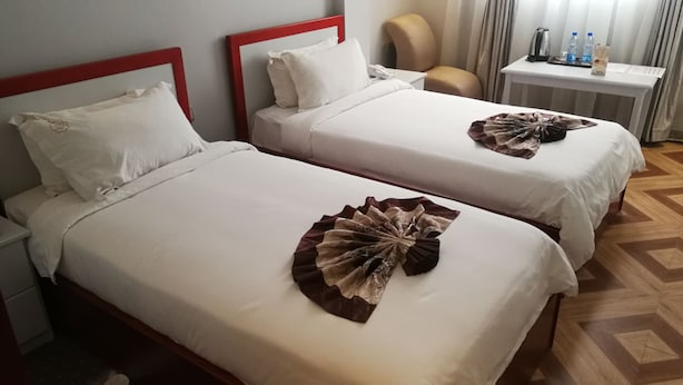 Two beds with white linens and red headboards, a bedside table with water bottles, and a chair. - Safe Addis Hotel and Spa (Addis Ababa)