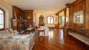 A spacious living room with wooden furniture, a fireplace, and large windows. - 300-square-meter villa · 6 bedrooms & 5 bathrooms · Cool in the summer (Bibbiena)