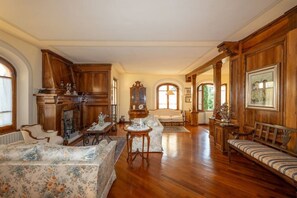 A spacious living room with wooden furniture, a fireplace, and large windows.