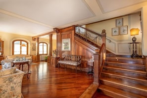 A spacious living room with a wooden staircase, a sofa, a bench, and a lamp.