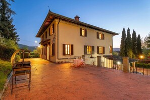 A two-story house with a patio, outdoor seating, and a view of the surrounding landscape.