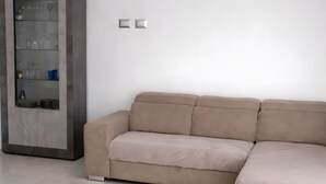 A beige sectional sofa in a modern living room with a glass cabinet and a tiled floor. - Apartment 'Perla' with Sea View, Balcony and Air Conditioning (Agrustos)