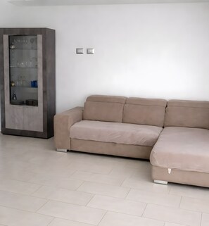 Ein beiges Ecksofa in einem modernen Wohnzimmer mit einer Glasvitrine und einem Fliesenboden.
