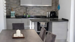 A modern kitchen with grey cabinets, a built-in oven, and a dining area with a table and chairs. - Apartment 'Perla' with Sea View, Balcony and Air Conditioning (Agrustos)
