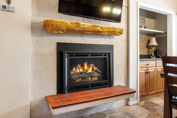 A fireplace with a TV mounted above it, a wooden shelf, and a tiled bench below.