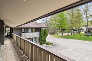 A balcony with a view of a residential street, a wooden deck, and a small tree.