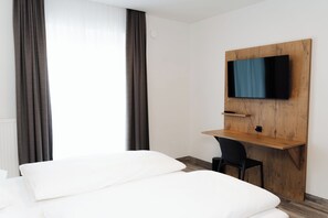 Hotellihuone, jossa on sänky, työpöytä, jossa on televisio, ja tuoli.