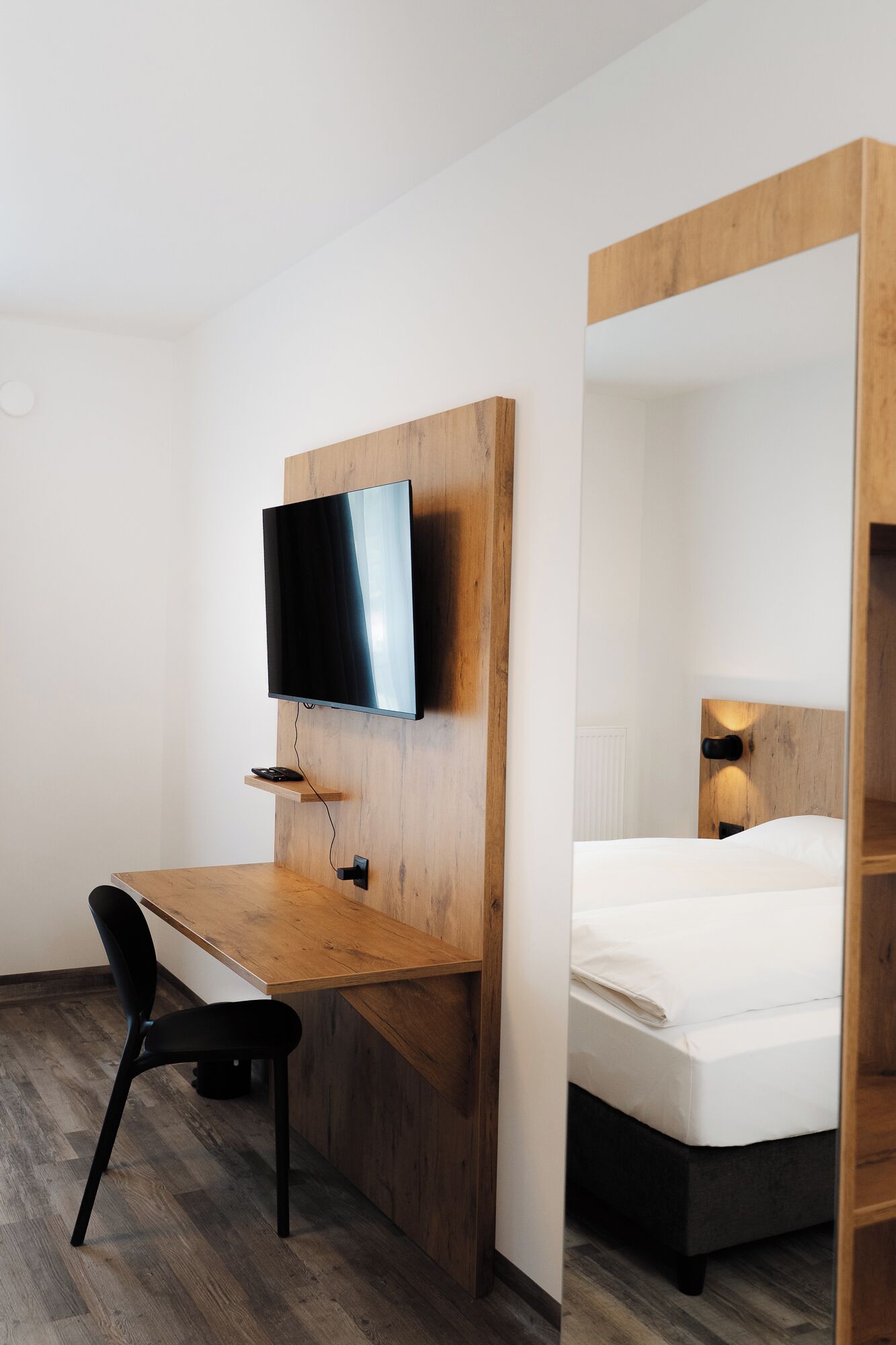 A compact hotel room with a wooden desk, a television, a bed, and a chair.