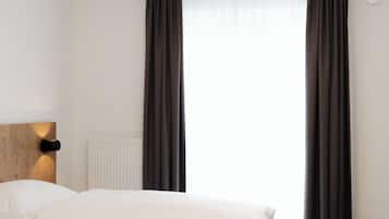 Habitación de hotel con cama, cabecera, lámpara de pared y ventana con cortinas.