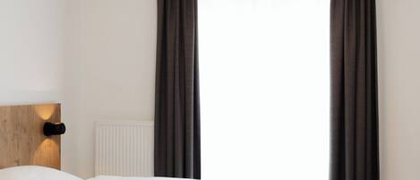 A hotel room with a bed, a headboard, a wall-mounted light, and a window with curtains.
