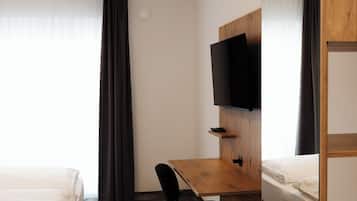 Habitación de hotel con cama, escritorio con silla, televisor montado en la pared y literas de madera.