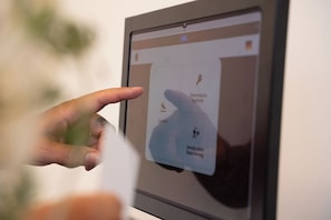 A hand interacting with a digital interface, possibly a check-in kiosk, with icons for check-in, room selection, and a map.