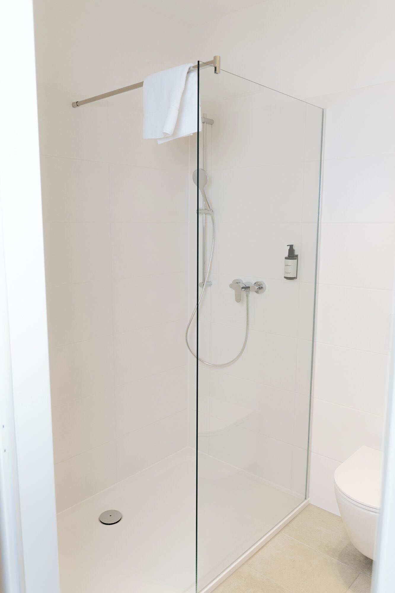 Eine Duschkabine mit Handbrause, ein am Wand montierter Wasserhahn und eine Toilette zur Rechten.