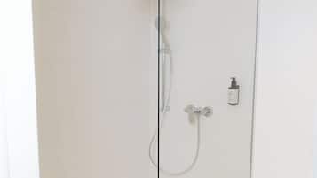 Eine Duschkabine mit Handbrause, ein am Wand montierter Wasserhahn und eine Toilette zur Rechten.