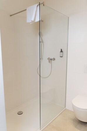 Eine Duschkabine mit Handbrause, ein weißes Handtuch auf einem Handtuchhalter und eine Toilette in einem modernen Badezimmer.