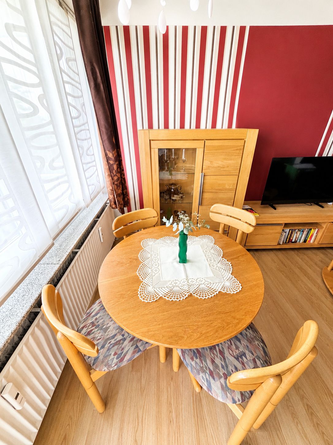 A dining area with a round wooden table, four chairs, a cabinet with glass doors, and a television on a stand.