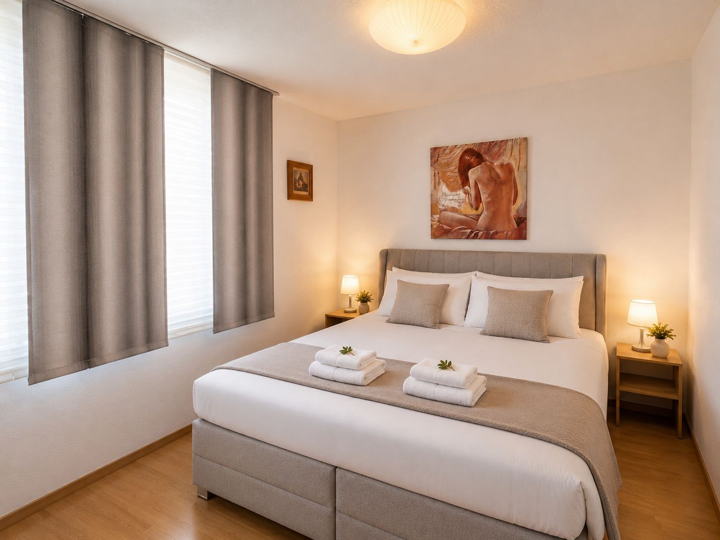A hotel room with a large bed, two bedside tables with lamps, a painting on the wall, and a window with curtains.