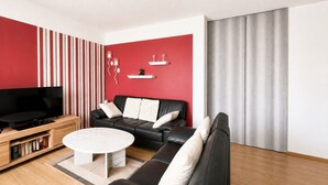 A modern living room with a black leather sofa, a white coffee table, a flat-screen TV, and a red accent wall.