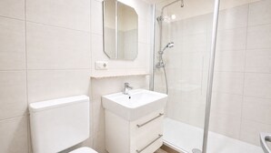 A bathroom with a toilet, sink, mirror, and glass-enclosed shower.