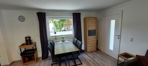 Ein kleiner Essbereich mit Tisch und Stühlen, einer Kaffeemaschine, einem Schrank und einem Fenster mit Vorhängen.