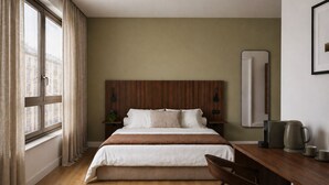Quarto de hotel com cama, cabeceira de madeira, mesas de cabeceira, escrivaninha com cafeteira e janela com cortinas.