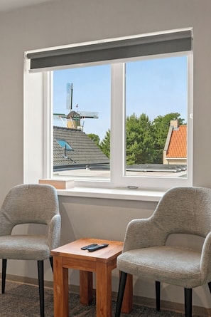 A room with two chairs, a small wooden table, and a window with a view of buildings and trees.