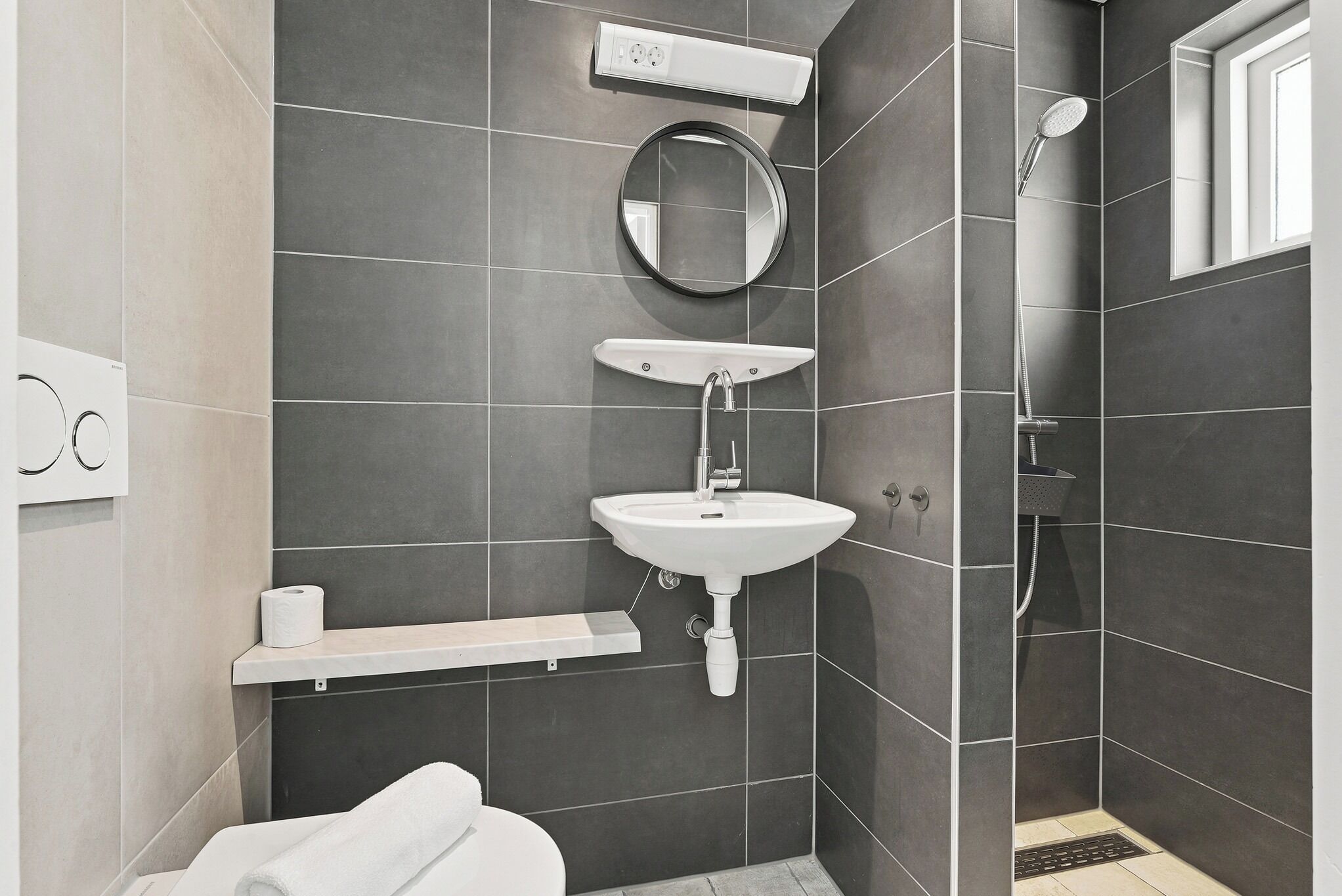 A modern bathroom with a white sink, a mirror, a towel, and a shower area.