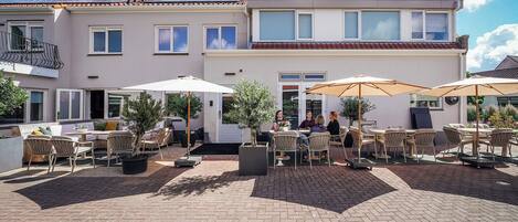 Ein zweistöckiges Gebäude mit einer Terrasse, die Sitzgelegenheiten und Sonnenschirme im Freien bietet.