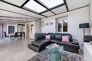 A modern living room with a sectional sofa, a glass coffee table, and a dining area with a white table and chairs. - Holiday Home “Lilas NO” with Terrace, Private Garden, and Wi-Fi (Barbâtre)