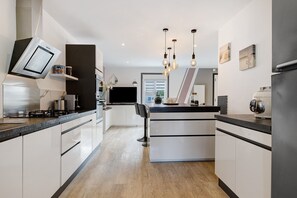 A modern kitchen with white cabinetry, a central island, and pendant lighting. - Holiday Home “Lilas NO” with Terrace, Private Garden, and Wi-Fi (Barbâtre)