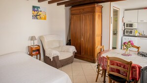 Een slaapkamer met een bed, een stoel, een kledingkast, een klein nachtkastje en een keukenhoek met een magnetron en kastjes.