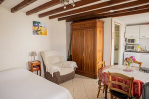Ein Schlafzimmer mit Bett, Stuhl, Schrank, einem kleinen Nachttisch und einer Küchenzeile inklusive Mikrowelle und Schränken.