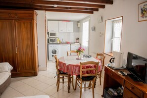 Ein Zimmer mit Esstisch, Stühlen, Fernseher, Schreibtisch, Kleiderschrank und einer Küchenzeile mit Geräten.