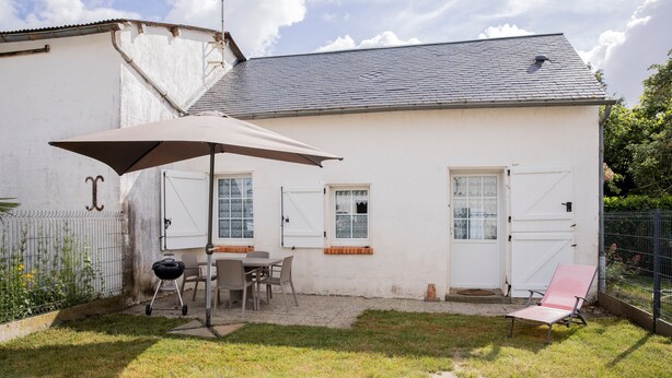 Een wit gebouw met een overdekte patio, een barbecue en een stoel.