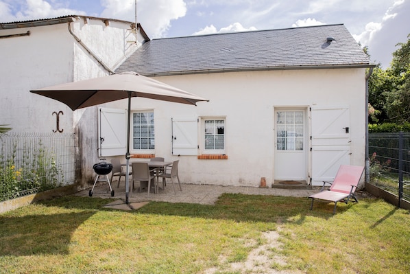Ein weißes Gebäude mit überdachter Terrasse, Grill und Stuhl.
