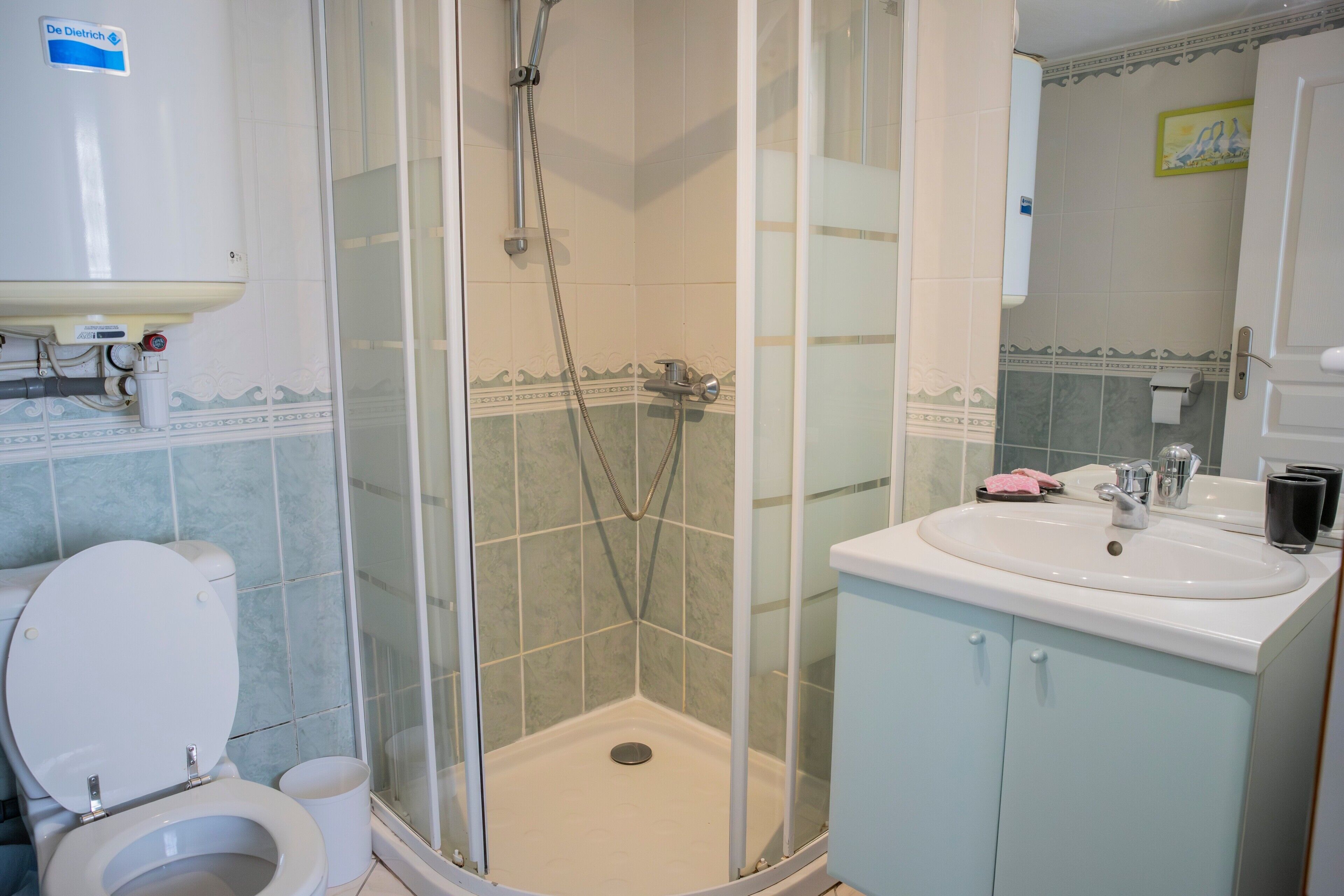 A bathroom with a toilet, shower, sink, and cabinet.
