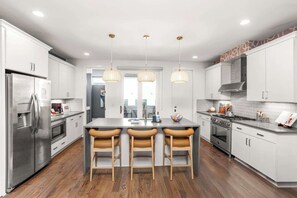 A modern kitchen with white cabinets, stainless steel appliances, a central island with bar stools, pendant lighting, and a view to the dining area. - 2 Units, Sleeps 24  Nashville's Best Location (Nashville)