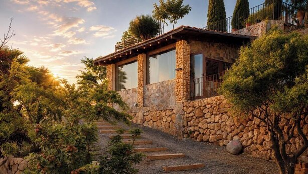Un bâtiment en pierre doté d’une terrasse en bois et d’un chemin de gravier menant à l’entrée.