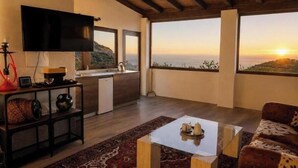 Un salon moderne doté d’un téléviseur à écran plat, d’un coin cuisine et d’un grand balcon offrant une vue sur le coucher de soleil.