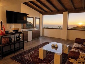 Ein modernes Wohnzimmer mit Flachbildfernseher, einer Küchenzeile und einem großen Balkon mit Sonnenuntergangsblick.