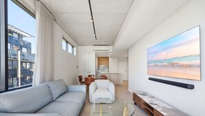 A modern living room with a sofa, a glass coffee table, and a painting of a beach scene. - Tranquil 2-Bed with Water View (Kingston)