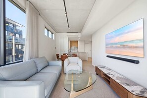 Ein modernes Wohnzimmer mit einer Couch, einem Glastisch und einem Bild von einer Strandansicht.