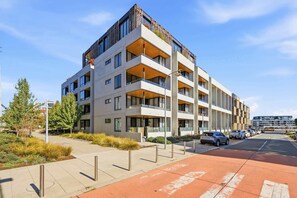 Ein mehrgeschossiges Wohngebäude mit Balkonen, einem Parkplatz und blauem Himmel.