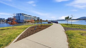A waterfront hotel with a concrete walkway, a lake, and modern buildings in the background. - Tranquil 2-Bed with Water View (Kingston)