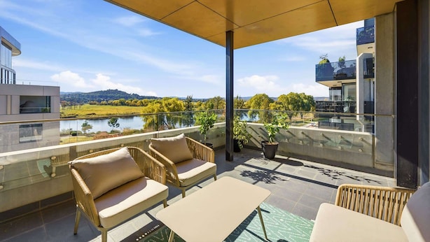 A balcony with wicker furniture, a glass table, and potted plants. - Tranquil 2-Bed with Water View (Kingston)