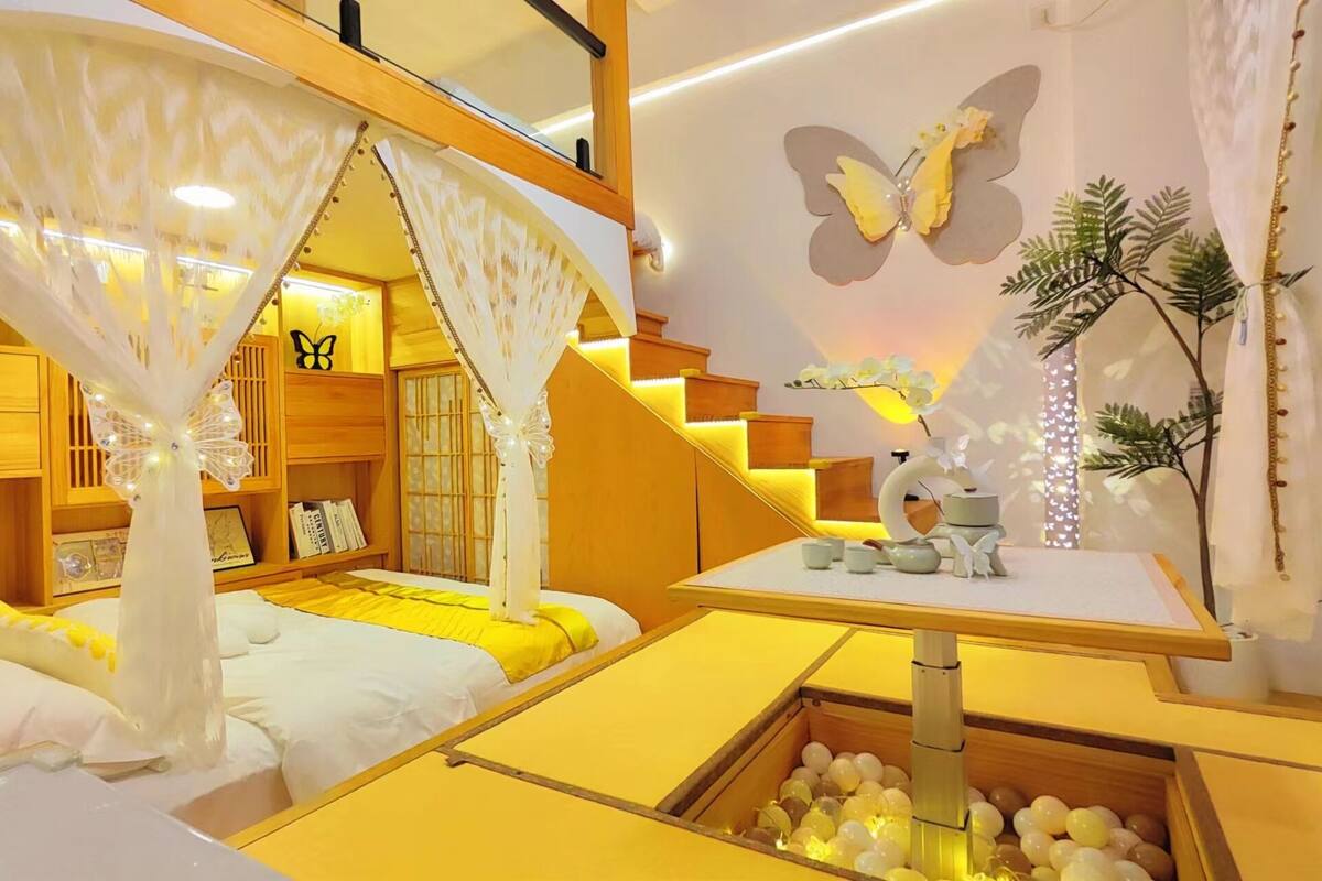 A room with a bed, a small table with decorative items, a staircase, and a wall with a butterfly decoration.